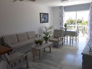 Ein Wohnzimmer mit einer Couch, Sesseln, einem Couchtisch und einem Balkon mit Tisch und Stühlen.
