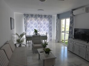 Ein Wohnzimmer mit einer Couch, einem Esstisch mit Stühlen, einem Fernseher und einer Topfpflanze.