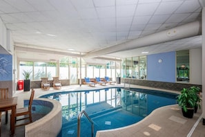 An indoor swimming pool with lounge chairs, a table, and potted plants.