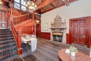 Eine prächtige Treppe führt zu einer oberen Ebene, ein Kamin mit Sims und ein Esstisch sind abgedeckt.
