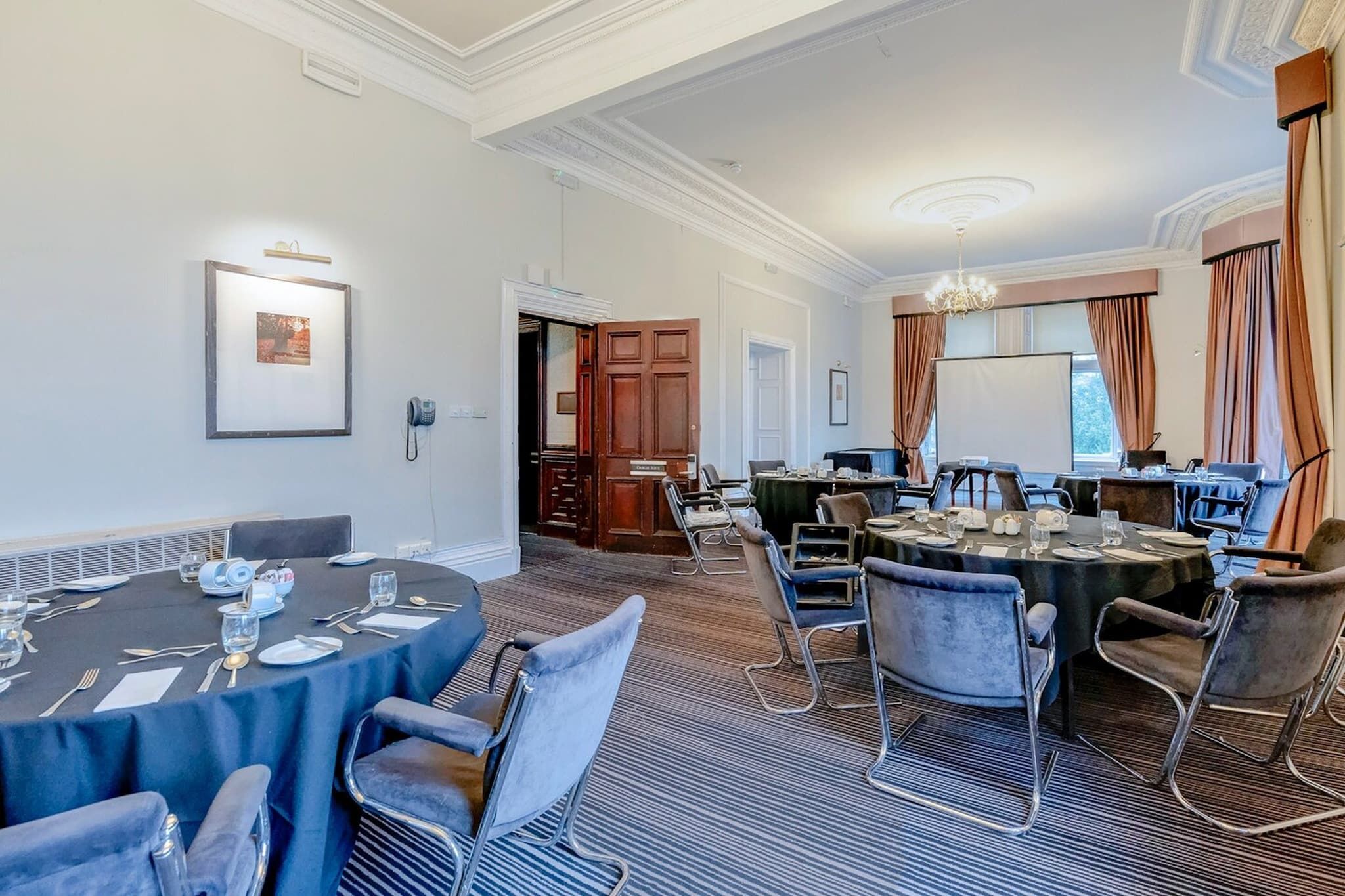 Une salle de conférence équipée de tables rondes, de chaises et d’un lustre.