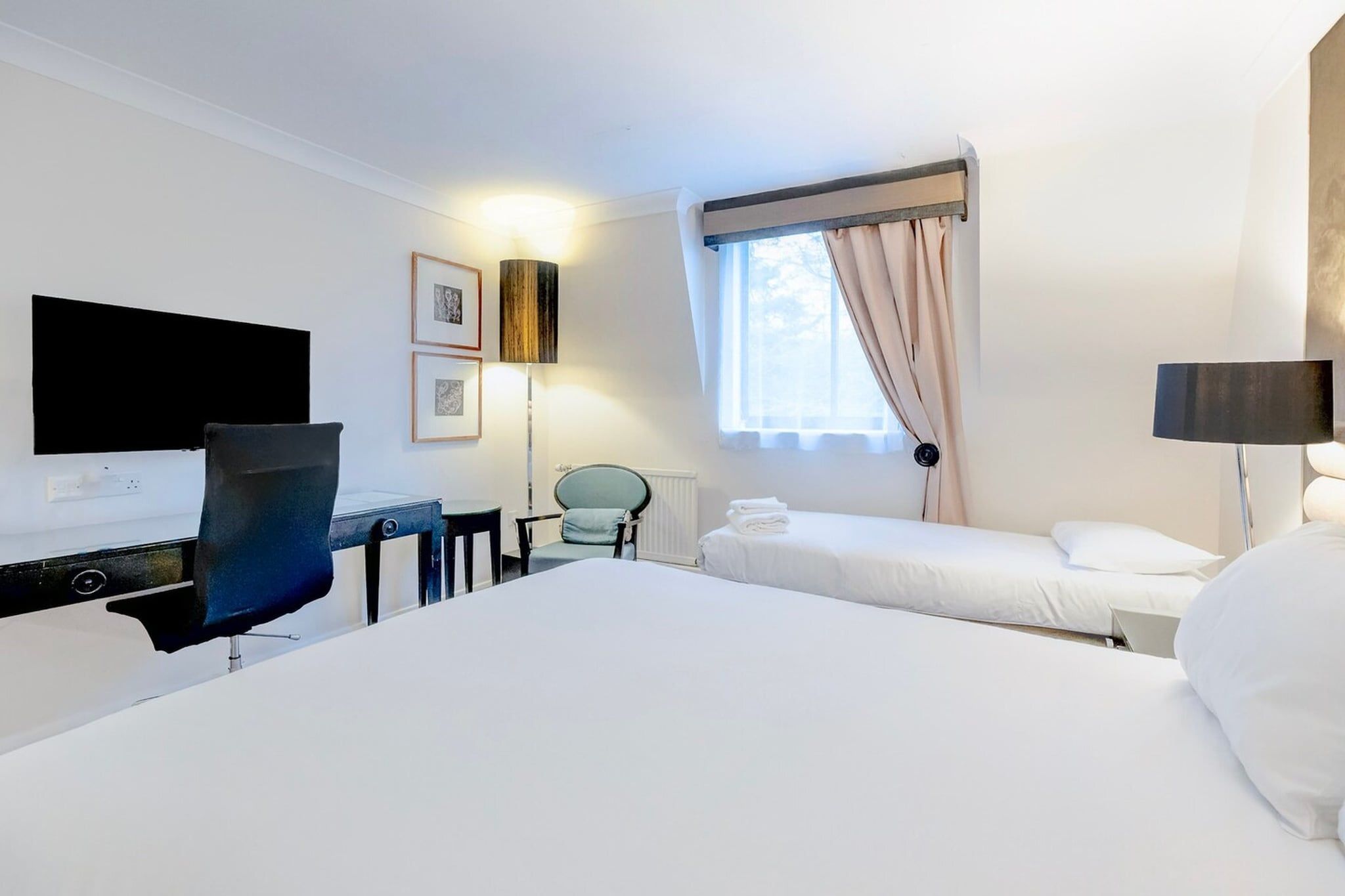 Ein Hotelzimmer mit einem großen Bett, einem Schreibtisch, einem Stuhl, einem Fernseher und einem Fenster mit Vorhängen.