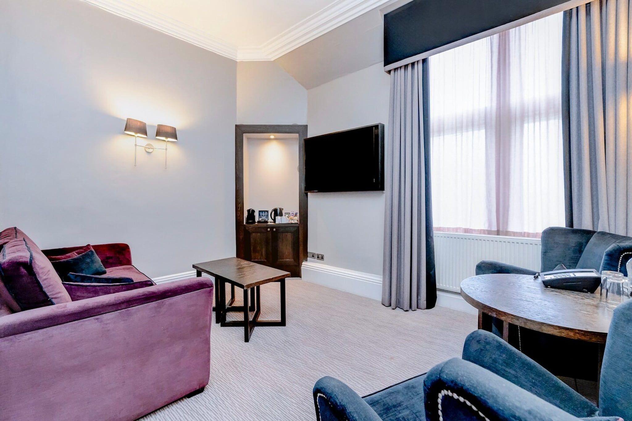 Ein modernes Hotelzimmer mit einer Couch, einem Sessel, einem Tisch und einem an der Wand befestigten Flachbildfernseher.