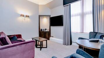 Ein modernes Hotelzimmer mit einer Couch, einem Sessel, einem Tisch und einem an der Wand befestigten Flachbildfernseher.