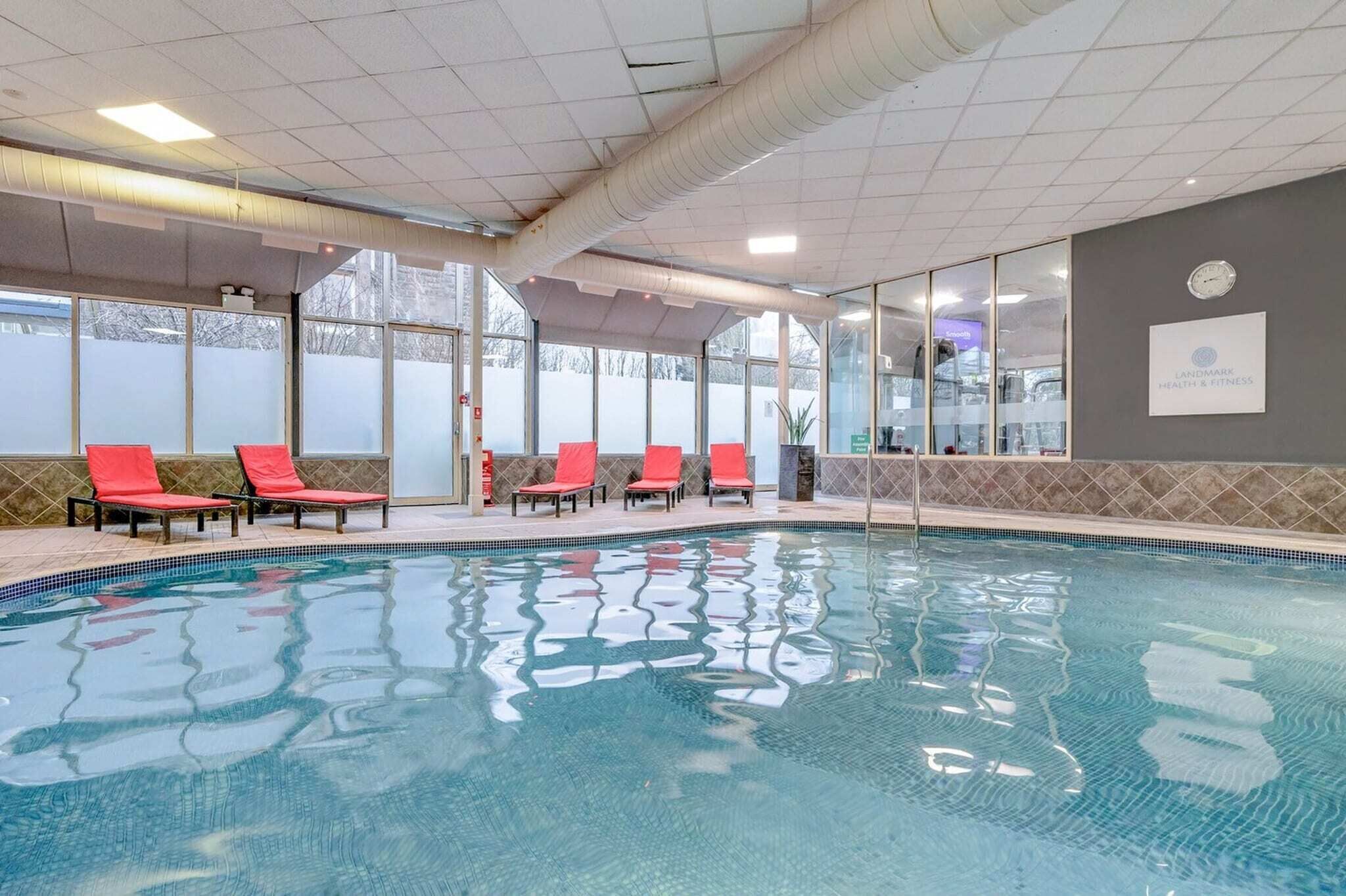 Una piscina con sillas rojas, un reloj y un cartel de Landmark Health & Fitness.
