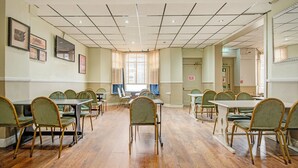 A conference room with multiple tables and chairs, a tiled ceiling, and framed artwork on the walls. - Standard Triple Room (Cardiff)