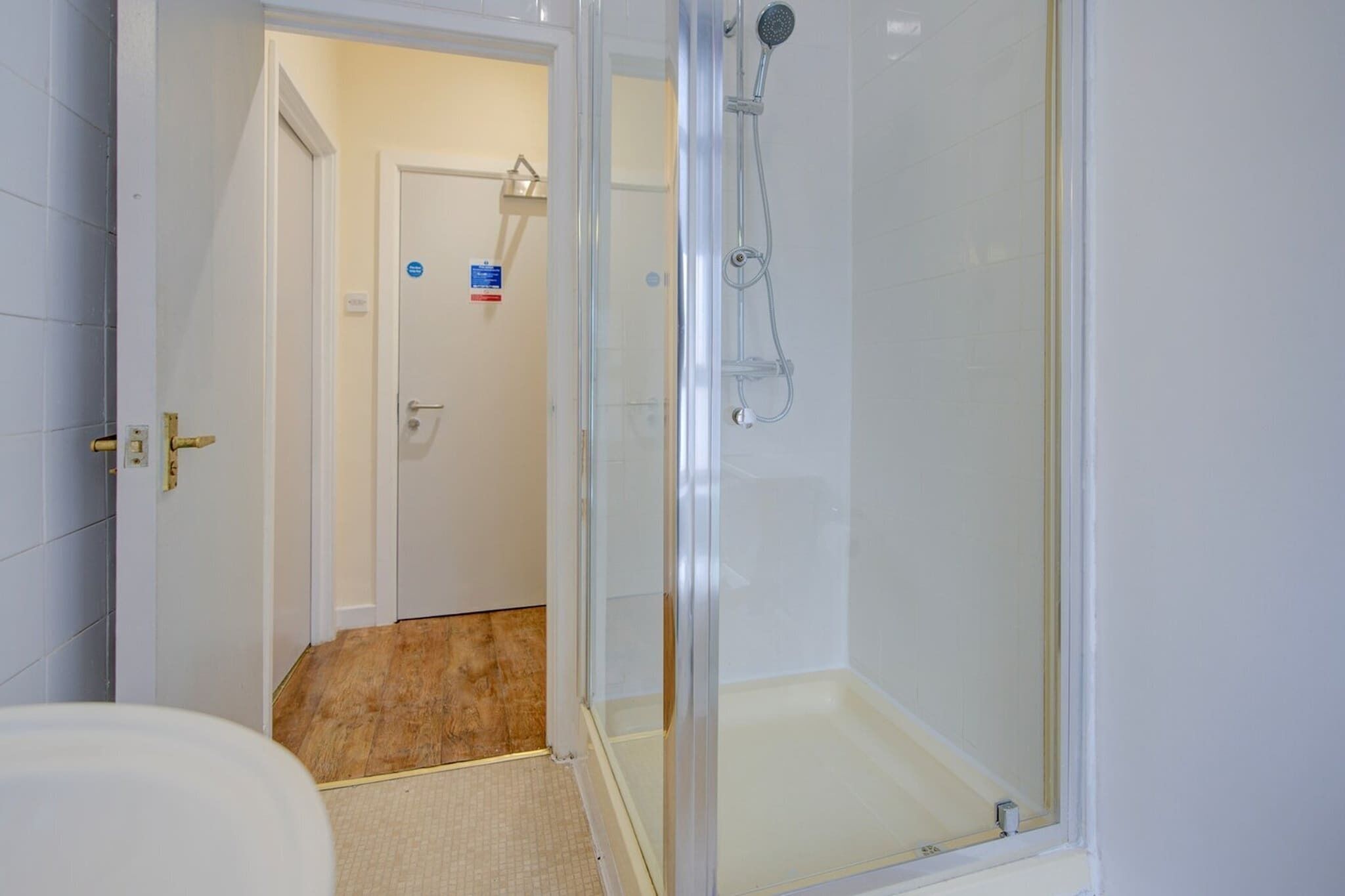 Un baño con ducha envuelta en vidrio, inodoro blanco y suelo de madera.