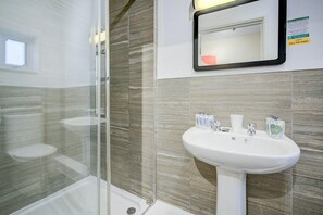Un bany modern amb plat de dutxa de vidre, un lavabo blanc amb productes de tocador i un mirall amb indicador de disponibilitat d'aigua calenta.