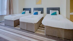 A hotel room with three single beds, each with a headboard, white bedding, and a towel on the bed. - Standard Triple Room (Cardiff)