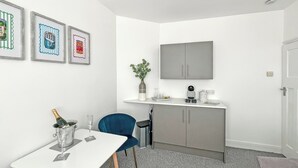 A small, modern room with a white table, a blue chair, a grey cabinet, and a mounted television. - 1 bedroom accommodation in Ely (Ely)