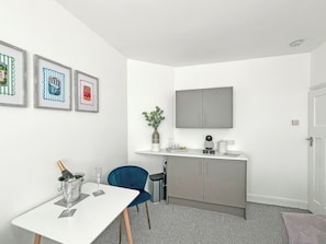A small, modern room with a white table, a blue chair, a grey cabinet, and a mounted television. - 1 bedroom accommodation in Ely (Ely)