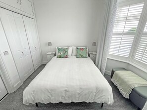 A bedroom with a bed, two nightstands, a window with blinds, a wardrobe, and a bench. - 1 bedroom accommodation in Ely (Ely)