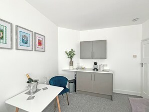 A small, modern room with a white table, a blue chair, a grey cabinet, and a mounted television. - 1 bedroom accommodation in Ely (Ely)