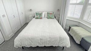 A bedroom with a bed, two nightstands, a window with blinds, a wardrobe, and a bench. - 1 bedroom accommodation in Ely (Ely)