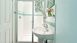 A bathroom with a glass shower enclosure, a white sink, and a mirror with a floral design. - 1 bedroom accommodation in Ely (Ely)