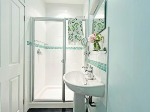 A bathroom with a glass shower enclosure, a white sink, and a mirror with a floral design. - 1 bedroom accommodation in Ely (Ely)
