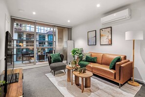 Ein modernes Wohnzimmer mit Sofa, Sessel, Couchtisch und einem großen Fenster mit Blick auf ein Gebäude.