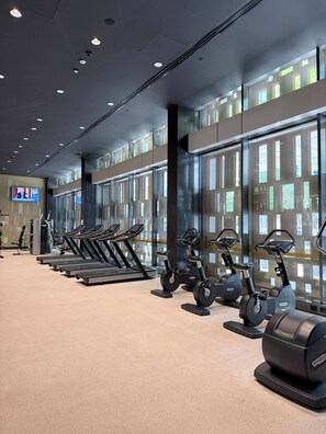 Ein Fitnessstudio mit Laufbändern, Ergometer und einem Fernseher, der einen Nachrichtensender zeigt.
