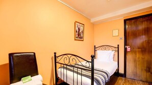 Ein Zimmer mit einem Bett, einem Stuhl, einer Holztür und einem gerahmten Bild an der Wand.