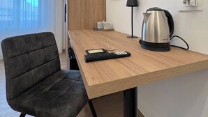 A modern hotel room with a wooden desk, a black chair, a flat-screen TV mounted on the wall, a coffee maker, and a lamp. - Elegant Suite between Sorrento and the Amalfi Coast (Castellammare di Stabia)