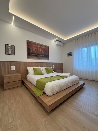 A modern bedroom with a wooden bed frame, a green throw blanket, and a large mural on the wall.. Elegant Suite between Sorrento and the Amalfi Coast