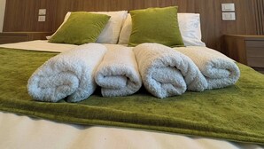 A hotel room with a bed, green and white pillows, a painting on the wall, and a neatly made bed with towels. - Elegant Suite between Sorrento and the Amalfi Coast (Castellammare di Stabia)