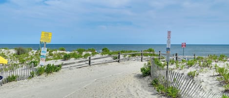 Una playa arenosa con una valla de madera, señalizaciones y vegetación escasa.