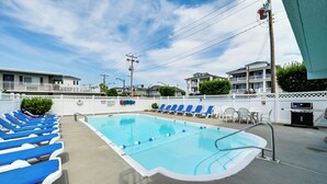 A swimming pool with blue lounge chairs, a white fence, and a building in the background. - Walk to Boardwalk & Beach! Ocean City Studio (Ocean City)