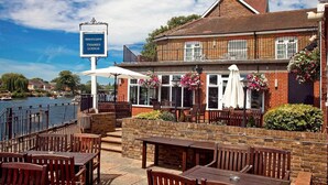 Ein Flussrestaurant mit Terrassensitzgelegenheiten, einem Schild mit der Aufschrift 'Mercure Thames Lodge' und Blick auf den Fluss.