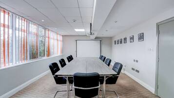 A conference room with a long table, chairs, a projector screen, and large windows with blinds.
