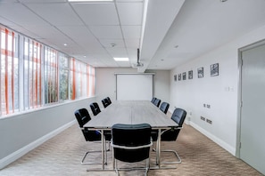 A conference room with a long table, chairs, a projector screen, and large windows with blinds. - Sunday London Staines-upon-Thames Heathrow T8 - Standard Family of 3 Room (London)