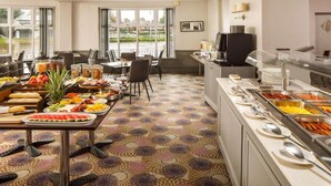 Ein Hotel-Speiseraum mit Frühstücksbuffet, Sitzmöglichkeiten und Blick durch die Fenster.