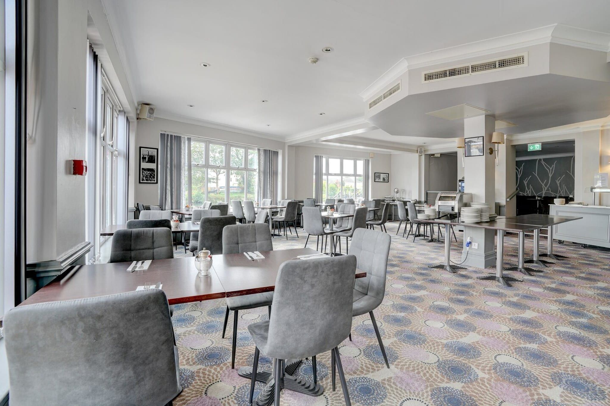 A spacious conference room with multiple tables and chairs, large windows, and a patterned carpet.