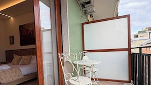 A balcony with a bed, a table, and chairs, an air conditioning unit, and a view of buildings. - Suite with balcony near Pompeii, Sorrento, and Amalfi (Castellammare di Stabia)