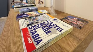 A room with a wooden table displaying magazines, a map, and a framed cityscape poster. - Suite with balcony near Pompeii, Sorrento, and Amalfi (Castellammare di Stabia)