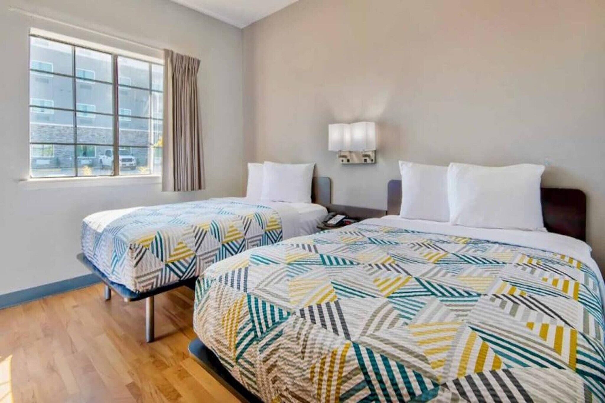 Une chambre d’hôtel avec deux lits, une grande fenêtre, une table de chevet et une lampe fixée au mur.