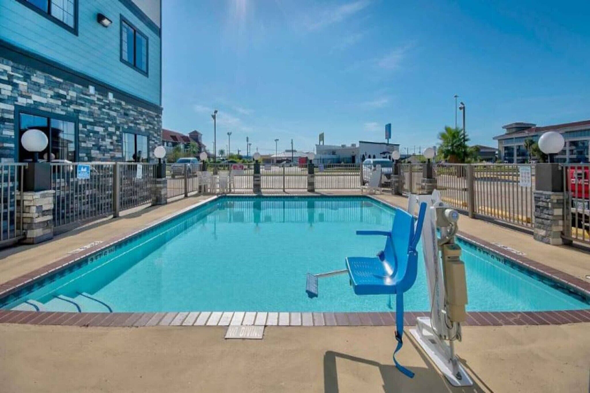 A swimming pool with a blue chair, surrounded by a fence, and a building with a blue facade in the background.