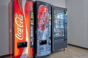 Tre försäljningsautomater med Coca-Cola-produkter står uppställda i en korridor.