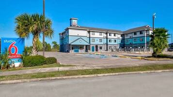 A multi-story hotel with a parking lot, a sign for Studio 6, and palm trees.