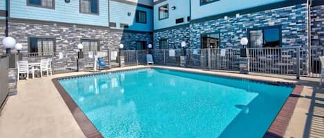 A swimming pool with a tiled deck, surrounded by a fence, and adjacent to a building with a stone facade.