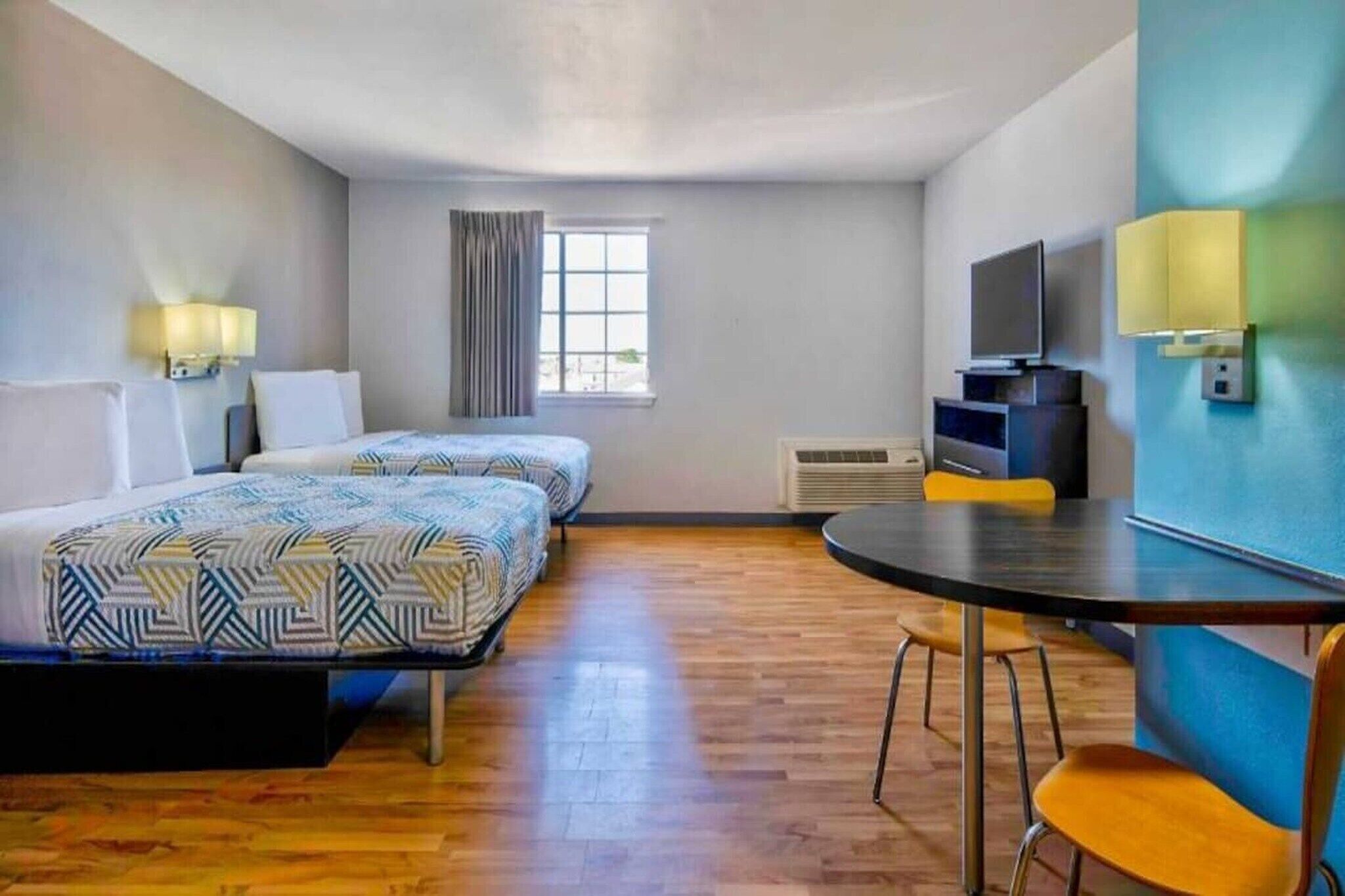 A hotel room with two beds, a dining table, a TV, and a window.