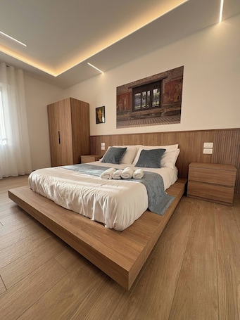 A modern bedroom with a large bed, wooden headboard, and a wall-mounted artwork.. Modern Suite between Pompeii and the Amalfi Coast