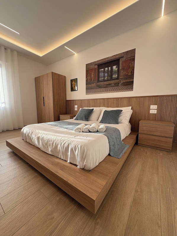 A modern bedroom with a large bed, wooden headboard, and a wall-mounted artwork. - Modern Suite between Pompeii and the Amalfi Coast (Castellammare di Stabia)