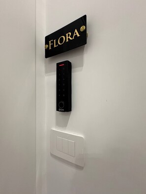 Ein an der Wand befestigtes elektronisches Gerät, eine Schilder mit der Aufschrift 'FLORA' und ein Lichtschalter.