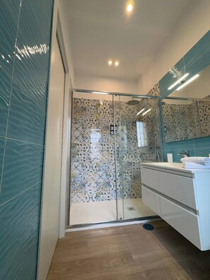 Een moderne badkamer met een douchecabine van glas, een witte wastafel met spiegel en een behang met patronen op de muren.