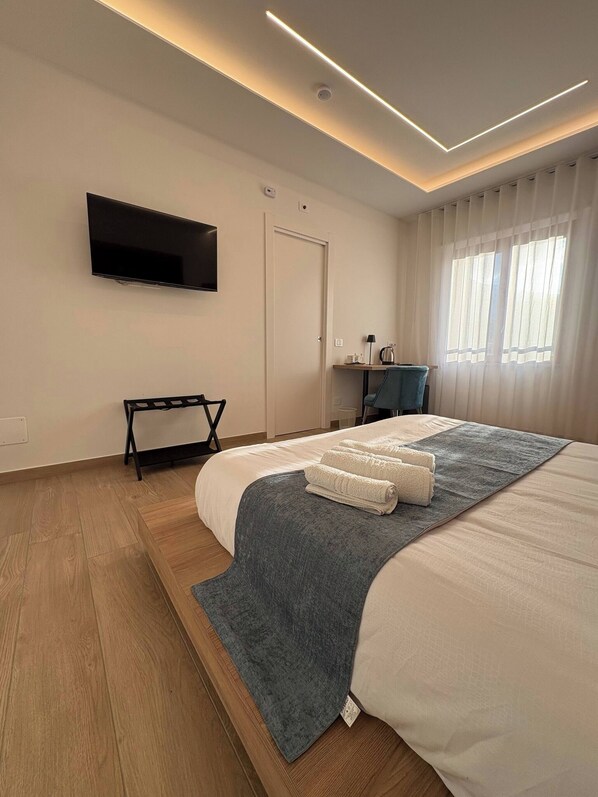 A modern hotel room with a large bed, a flat-screen TV, a desk with a chair, and a window with curtains. - Modern Suite between Pompeii and the Amalfi Coast (Castellammare di Stabia)
