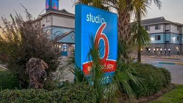 A large blue sign with 'studio 6' and 'stay' text, surrounded by greenery and a building in the background.
