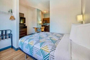 Una habitación de hotel pequeña con una cama, un pequeño espacio kitchenette, un televisor y un escritorio.