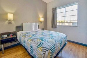 Quarto de hotel com cama, mesa de cabeceira, abajur e janela com cortinas.