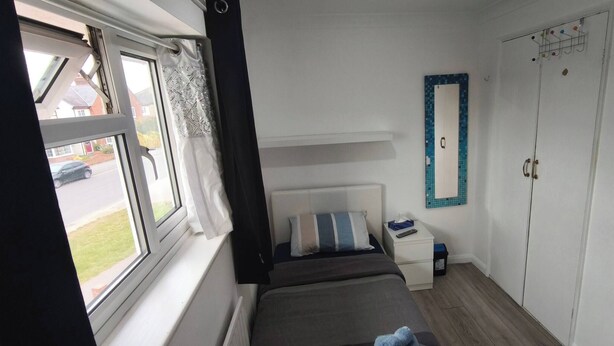 A bedroom with a bed, a bedside table, a wardrobe, and a window with curtains. - Small Cozy Room in Chelmsford Springfield (Springfield)